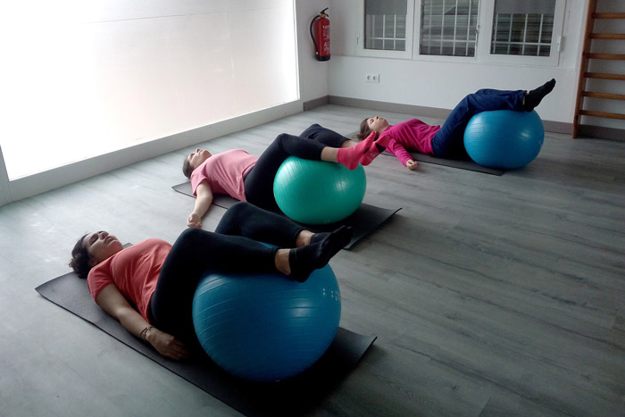 Tres chicas estiradas en su esterilla y con los pies encima de una pelota de pilates