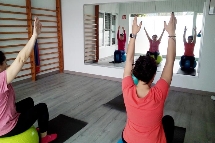 Tres chicas sentadas cada una en una pelota de pilates y con las manos levantadas